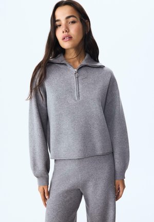 Pullover grigio con zip in morbido tessuto a maglia, dotato di un colletto alto e di una cerniera a cerchio, caratterizzato da una vestibilità comoda e da polsini a costine.