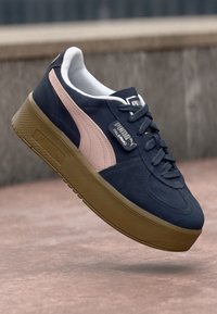 Navy suede sneaker with pink side stripe, round toe, and thick brown rubber sole. Features black logo tag and lace-up front.