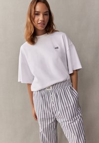 Vit oversized t-shirt med svart "self." broderi, kombinerad med grårandiga, avslappnade byxor med knappöppning fram och elastisk midja.