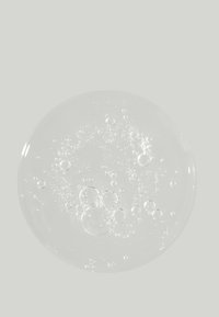 Grosse bulle de savon claire remplie de petites bulles, se détachant sur un fond gris clair, mettant en valeur la transparence et la texture liquide.