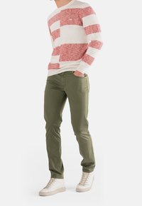 Maglione a righe rosse e bianche, pantaloni verdi e sneakers bianche; abbigliamento casual, texture a maglia sopra, tessuto liscio per i pantaloni.