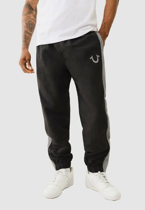 Zwarte joggers met grijze zijkanten, elastische boorden en een subtiele logo-opdruk op de voorzak. Lichtgewicht stof met een gladde textuur.