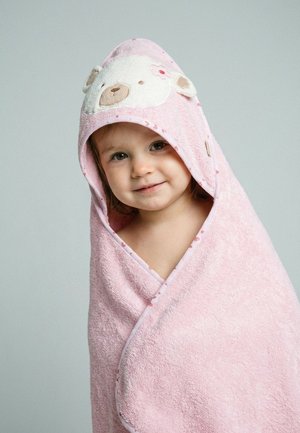Tout-petit enveloppé dans une serviette à capuche rose avec un motif de visage d'ours, souriant doucement sur un fond gris uni.