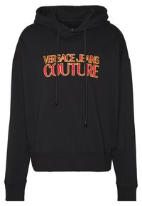 Svart hoodie med dragsko, med fet röd och gul "VERSACE JEANS COUTURE" text över framsidan. Mjuk tyg, avslappnad passform.