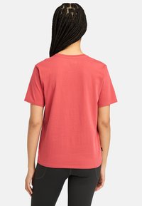 T-shirt en coton corail à manches courtes avec col rond ; coupe décontractée ; texture lisse ; couture visible le long de l'ourlet ; associé à des leggings noirs.