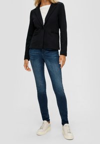 Mustat räätälöidyt bleiserit, joissa on yksittäinen nappi, yhdistetty sinisiin farkkuihin ja valkoisiin tennareihin. Silkkinen kangas, slim fit -leikkaus ja tavalliset kaulukset.