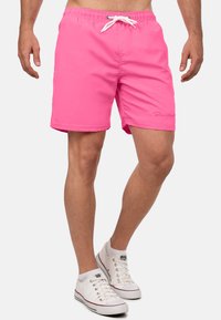 Shorts de bain roses en tissu léger, dotés d'une taille élastique avec un cordon blanc et d'un petit logo sur le côté.