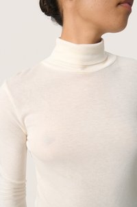 Light cream turtleneck top made of a soft, thin fabric; fitted design with long sleeves and a smooth texture. Subtle variations in color.