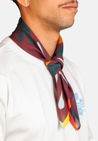 Hombre con una camisa blanca y una bufanda de patrón multicolor atada alrededor de su cuello.