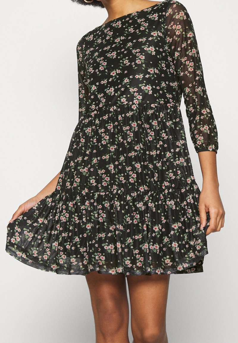 Robe noire à fleurs avec des manches trois-quarts en dentelle transparente, un bas plissé et de petits motifs floraux roses et verts tout au long. Tissu doux et léger.