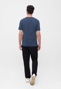 Dunkelblaues Kurzarm-T-Shirt mit Rundhalsausschnitt, kombiniert mit schwarzen Hosen und weißen Turnschuhen, von hinten betrachtet.