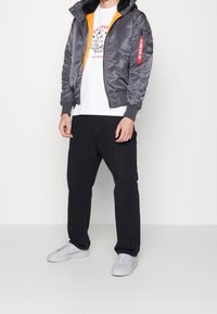 Šedá bomber bunda s oranžovou podšívkou, vybavená kapsou na zip a žebrovanými manžetami, kombinovaná s bílým tričkem, černými kalhotami a bílými teniskami.