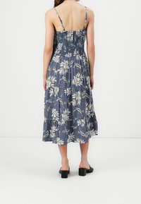 Blaues Midi-Kleid mit floralen Mustern, Spaghetti-Trägern, Raffung im Oberteil und gestuftem Rock. Kombiniert mit schwarzen Blockabsatzsandalen.