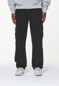 Svart cargobyxor i tyg, med flera fickor, avslappnad passform och en något lös design. I kombination med grå sneakers.