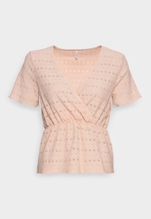 Lyserød kortærmet bluse med hullestof, V-udskæring i omslagsstil, indsnøret talje og diskret blomstermønster med udskæringer.