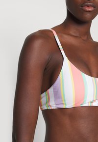 Pestrý pruhovaný bikiny top s tenkými popruhmi, so trojuholníkovým tvarom, jemnou tkaninou a zmesou pastelových farieb vrátane ružovej, žltej a zelenej.