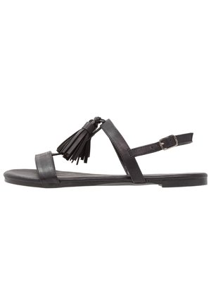 Czarne skórzane sandały z płaską podeszwą, pojedynczym paskiem na palcach, paskiem wokół kostki z klamrą oraz dekoracyjnymi frędzelkami po bokach.