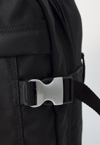 Black backpack featuring a textured material, adjustable strap, and a silver buckle for secure closure. Minimalist design with no patterns.