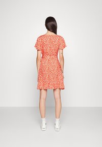 Rotes Kleid mit weißem Blumenmuster, kurzen Rüschenärmeln, tailliertem Schnitt und schwingendem Rock, kombiniert mit weißen Stiefeletten.