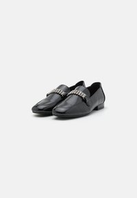 Chaussures à enfiler en cuir noir avec un talon plat, une texture lisse et un ornement en cristal décoratif sur le devant supérieur.