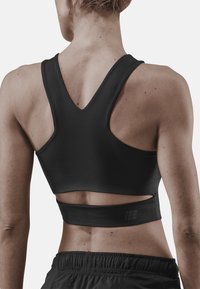 Reggiseno sportivo nero con design a V sulla schiena, texture liscia e dettagli ritagliati nella parte inferiore. È abbinato a pantaloni corti scuri.