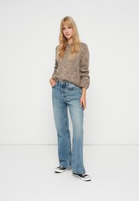 Bézs barna pulóver texturált felülettel, világoskék egyenes szárú farmernadrággal párosítva. Fekete sportcipőkkel egészül ki az öltözet.