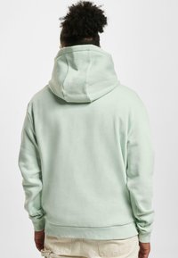 Felpa verde menta con un ampio e morbido cappuccio. Presenta polsini e orlo a coste, e una texture liscia. Design semplice, senza loghi o motivi visibili.