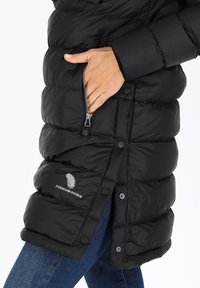 Svart vadderad jacka med en dragkedjeficka, tryckknappar och en logotyp tryckt på den nedre framsidan. Mjuk, texturerad material med ett quiltat mönster.