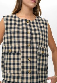 Weste aus Stoff in Creme und Marine. Mit Rundhalsausschnitt, knöpfbarer Vorderseite und zwei Brusttaschen mit Knopfklappen.