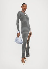 Long gray striped dress with a fitted design, button closure, side slit, and cream-colored trim. Model holds a light blue pouch bag.