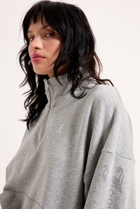 Γκρι φούτερ με ψηλό γιακά, ασημί φερμουάρ και λεπτομέρειες από στρας στο στήθος και το μανίκι. Μαλακή υφή, oversized εφαρμογή.