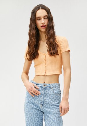 Kortärmad, ribbad croptop i persikofärg med knäppning. Kombination med ljusblå jeans med blommönster.
