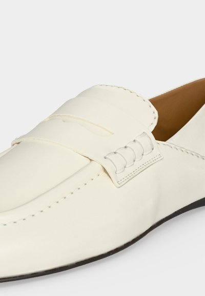 Άσπρο δερμάτινο loafer με ραμμένο λουράκι penny και καφέ εσωτερικό, με κομψή μαύρη σόλα και λεπτομερή ραφή κατά μήκος των άκρων.