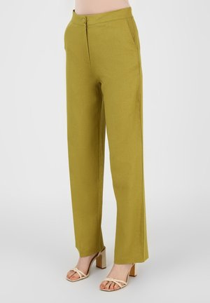 Grüne, hoch taillierte Hose aus strukturiertem Stoff mit seitlichen Taschen und einem Knopfverschluss, kombiniert mit beigen Sandalen mit Blockabsätzen.