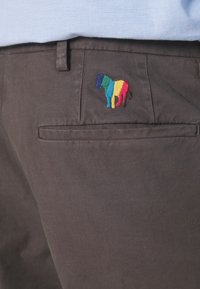 Gros plan sur la poche d'un pantalon foncé avec un petit cheval brodé aux rayures bleu, vert, jaune et rouge.