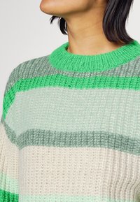 Sweter z dzianiny z okrągłym zielonym dekoltem, z poziomymi paskami w jasnym zielonym, ciemnozielonym i kremowym kolorze oraz teksturowanym wykończeniem.