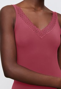 V-neck camisole in dusty rose, featuring a textured lace trim along the neckline. Smooth fabric and slim-fit design, highlighting the silhouette.