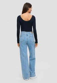 Marineblauwe long-sleeve top met een brede rughalslijn, gecombineerd met hooggeriemde lichtblauwe cargobroeken met zijzakken en een ontspannen pasvorm.