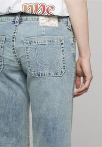 Světle modré džínové kalhoty s volnějším střihem, se zdvojeným prošitím zadních kapes s obloukovým designem a tkanou štítkem na pásku.