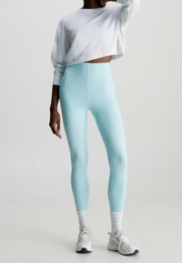Light blue leggings made of stretchy fabric, paired with a cropped white sweatshirt and white socks, worn with grey and white sneakers.