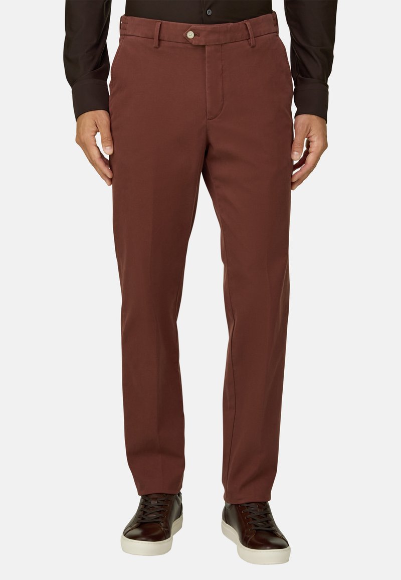 Homme portant un pantalon marron coupe droite, une chemise noire et des baskets marron foncé à lacets avec semelles blanches, debout devant un fond uni.