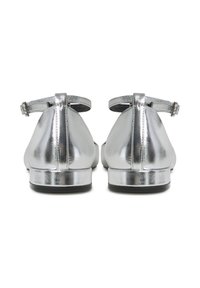 Par sjajnih srebrnih ravnih cipela s remenčićima oko gležnja, gledano s leđa na bijeloj pozadini.