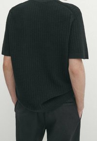 Mustaa neulepaitaa lyhyillä hihoilla, jossa on teksturoitu kuvio, ribattu kaula-aukko ja kaareva helma takana.