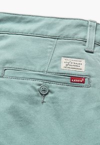 Ljus turkos denimbyxor med en bakficka, knäppning med knapp och en vävd varumärkesetikett med "LEVI STRAUSS" och "the two horse brand."