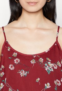 Top floral burdeos con tirantes finos, que presenta un patrón floral en rosa y verde. Tejido suave y ligero con un escote redondeado.