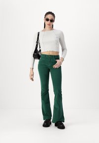 Crochet-trimmed, long-sleeve white top paired with green flared corduroy pants and black platform shoes, accessorized with a black bag.