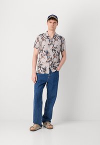 Short-sleeve shirt with a light grey background and multicolored horse print, paired with blue denim pants and brown slide sandals.