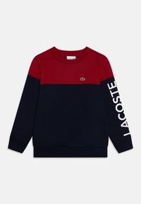 Langarm-Sweatshirt mit rotem oberen Abschnitt, marineblauem unteren Abschnitt, kleinem grünen Krokodil-Logo auf der Brust und "LACOSTE"-Text am rechten Ärmel.