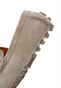 Zapato mocasín de ante beige con punta redondeada y suela de goma texturizada que presenta tacos de tracción cuadrados en el borde. Detalles de costura mínimos.