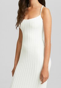 Robe blanche sans manches, en matière texturée côtelée, silhouette ajustée, avec bretelles réglables. Aucun motif ou accent visible.